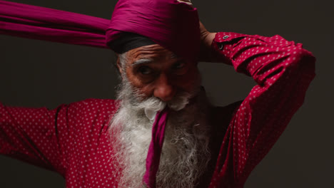 Low-Key-Studio-Lighting-Shot-Of-Senior-Sikh-Man-With-Beard-Tying-Fabric-For-Turban-Against-Dark-Background-1